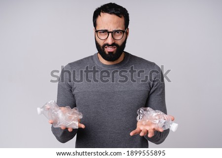 Disappointed young Arabic man holding plastic bottles isolated over grey background