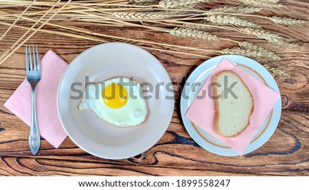 Still life with the image of breakfast in a rural house: egg omelet and bread on plates, fork, paper napkins. Everything is on a table made of old boards on which there are ears of wheat 