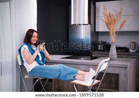 Shopping or ordering delivery online with mobile smart phone. Happy young woman using cellphone at home while sitting on a kitchen.