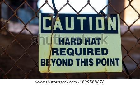 Worn out hard hat warning sign on a rusted fence at a construction site