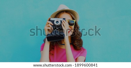 Summer portrait of young woman photographer with vintage film camera on a blue background