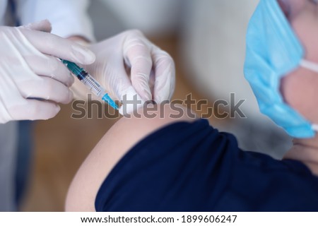 Young Female doctor in protective mask injecting or prepairing for injecting vaccine against coronavirus or ncov 19 or covid into patient's arm Royalty-Free Stock Photo #1899606247