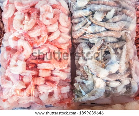 Two large plastic bags of frozen raw and cooked shrimp, on the counter of the fish market. Royalty-Free Stock Photo #1899639646