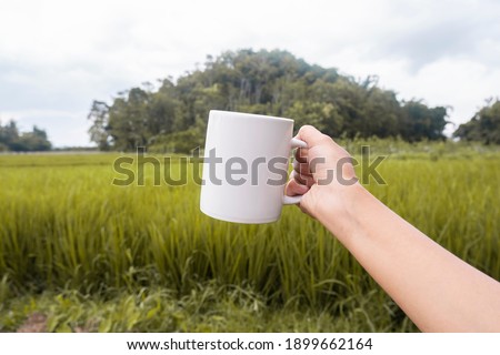 Mug mockup, a white mug on the ground with a natural view of rice plants and hills. Great for layering your custom quotes and designs for selling mugs.