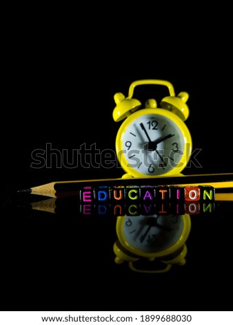 Selective focus.Word EDUCATION from a black dice with pencil and blur clock on a black back background.Shot were noise and film grain.