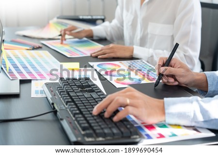 graphic designer team working on web design using color swatches editing artwork using tablet and a stylus at desks In creative office.