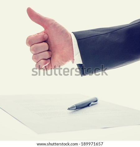 Retro vintage effect image of the arm of a businessman giving a thumbs up gesture of approval , success and agreement with a document and pen below conceptual of a business deal.