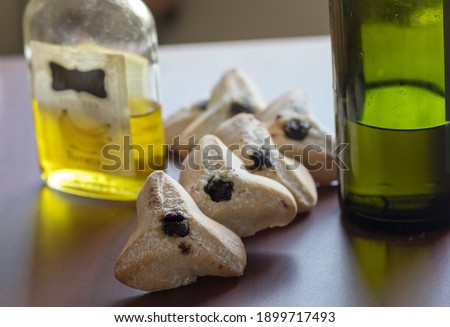 Triangular pastry made from crispy dough stuffed. Traditional Jewish food for Purim. Located on a wooden surface next to glass bottles