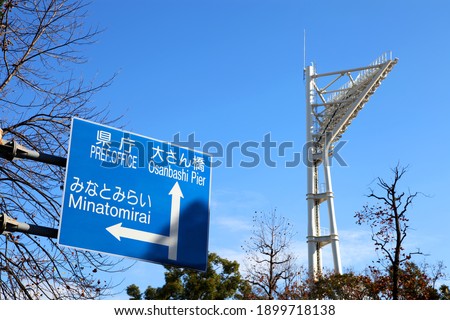 A large road sign with the floodlights of  Yokohama stadium in the background.