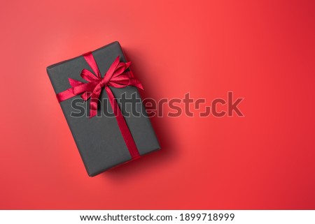 Black gift box with red bow on red background top view, Valentines day, Flat lay style with copy space.