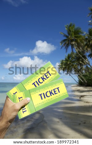 Hand holding pair of Brazil tickets in front of tropical palm trees with shadows on remote Nordeste Bahia beach