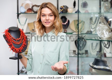 Portrait of young salesgirl of jewelry boutique offering necklaces of natural precious corals Royalty-Free Stock Photo #1899727825
