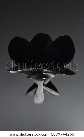 Artistic bucket flower form made with spoons and reflection isolated on dark background