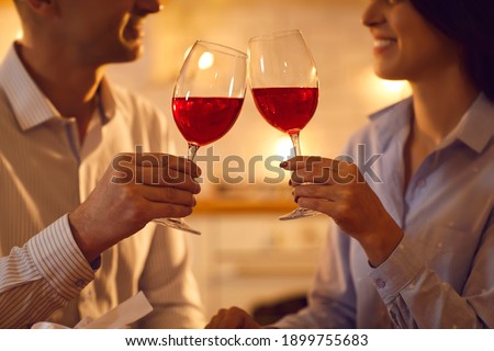 Cropped shot of happy married couple raising toast on romantic date at home. Man and woman in love drinking red wine on rendezvous in the evening. Hands clinking glasses closeup, soft selective focus Royalty-Free Stock Photo #1899755683