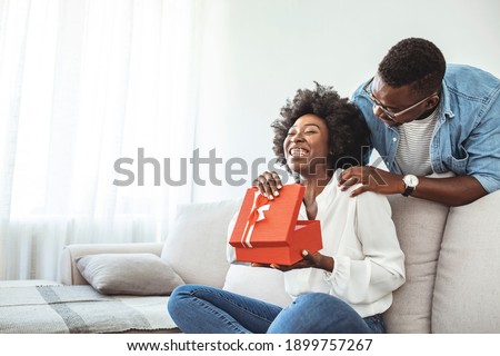 Beautiful young couple at home. Hugging, kissing and enjoying spending time together while celebrating Saint Valentine's Day with gift box in hand. Man giving a surprise gift to woman at home
