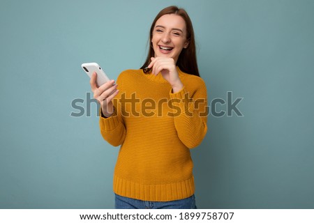 Photo shot of attractive positive good looking young woman wearing casual stylish outfit laughing poising isolated on background with empty space holding in hand and using mobile phone messaging sms