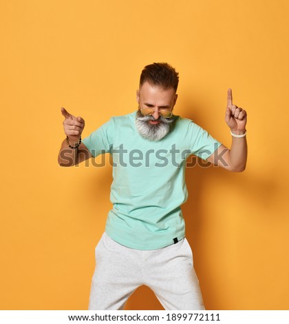 Active lifestyle. Stylish modern and cool funky trendy gray-haired hipster guy dancing and having fun on bright orange background. Concept of elderly people lifestyle. Isolated.