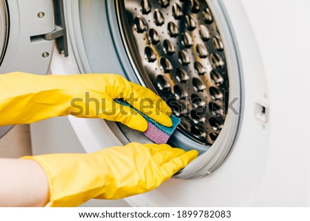A man in yellow gloves cleans a dirty, moldy rubber seal on a washing machine. Mold, dirt, limescale in the washing machine. Periodic maintenance of household appliances. Royalty-Free Stock Photo #1899782083