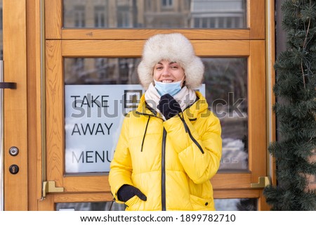 Happy young woman at the door of the restaurant on a cold winter day, lettering, takeaway food.