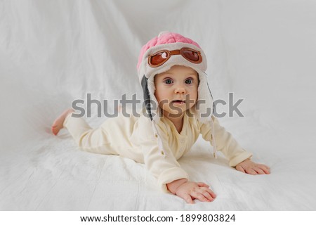 Сute infant wearing pilot hat lying on white background  pretending being pilot