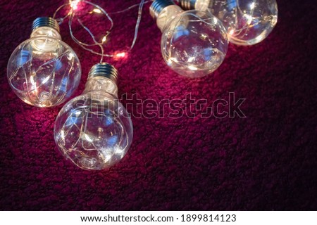 Garland of light bulbs close-up lies on a textile raspberry background close-up light-coloured in dark tones with a blurry focus