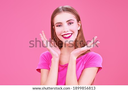 Happy girl teenager in a pink t-shirt smiling at camera on a pink background. Youth style. Cosmetics and make-up.