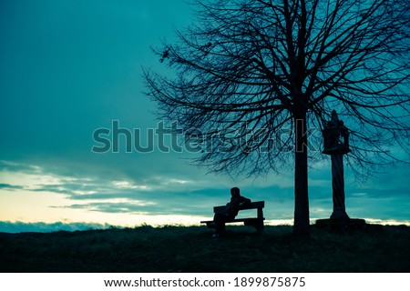 silhouette of a mysterious hacker. Silhouette portrait of a lonely anonymous man sitting on a bench as dark clouds above him roll, with the sun beginning to set behind  Royalty-Free Stock Photo #1899875875