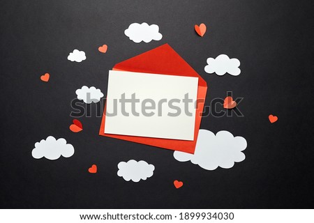 Valentines day greeting card mockup with paper decorations on black background. Blank greeting card or invitation and white paper clouds, red envelope and hearts