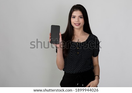 Happy young pretty female smiling at camera, holding mobile phone,  showing something interesting and exciting on mobile phone with copy space for your text or advertising content.