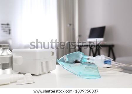 Modern nebulizer with face mask and medicines on white table indoors. Equipment for inhalation