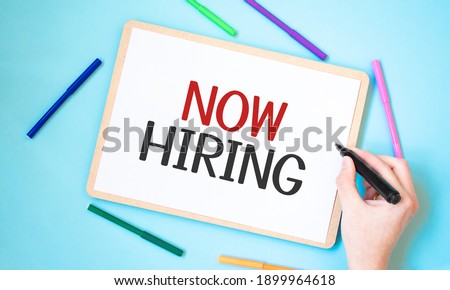 Text now hiring on a notebook surrounded by colored felt-tip pens, business concept idea,