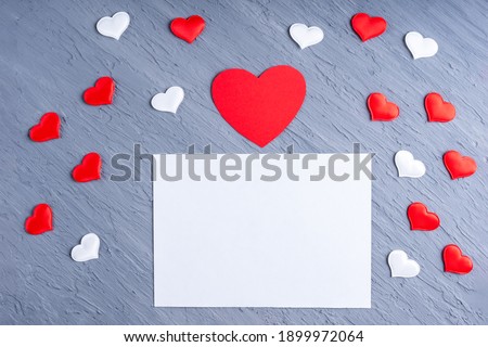 Love letter, valentine card for loved ones. Blank white sheet of paper surrounded by white and red heart shapes on gray trending background, copy space, top view. Valentines day concept