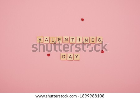 Message "Valentines Day" made from wooden tiles and three red love hearts on a pink background