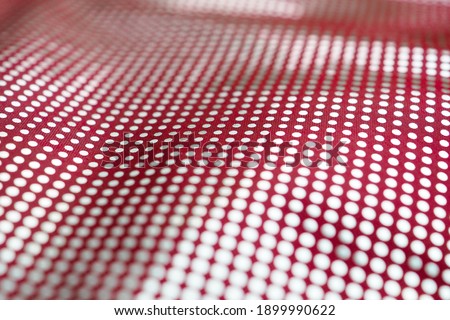 Selective focus on the surface of a red textile fabric with a pattern of small round silver dots. Abstract background with strong blur.