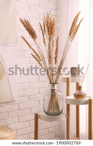 Fluffy reed plumes near white brick wall indoors. Interior element