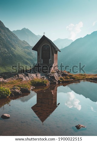 A vertical shot of a small church by the water with mountains in the background