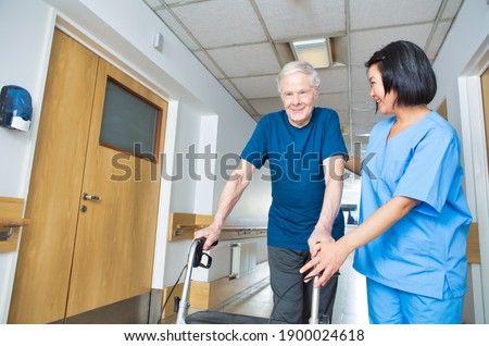 Asian nurse assisting elderly man with walker walking on the hospital floor. Royalty-Free Stock Photo #1900024618