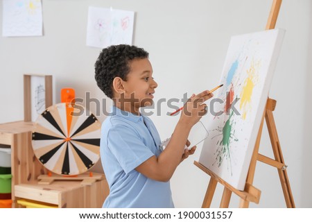 Cute African-American boy painting at school