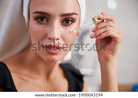 Close-up photo of a calm young lady with perfect skin using hyaluronic acid to moisturize her face