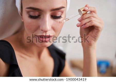 Close-up photo of young woman applying moisturizing product to her face by using a pipette