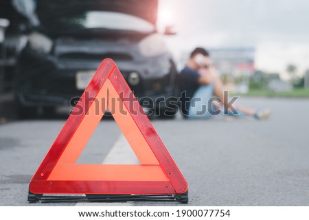Red warning triangle with a broken down car,Emergency triangle on the road, stopped car and man calling by phone in the background.