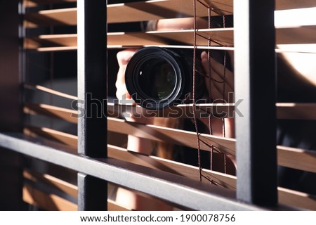 Private detective with camera spying near window indoors, closeup