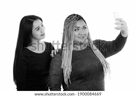 Young happy fat Asian woman and Asian transgender woman smiling while taking selfie picture with mobile phone