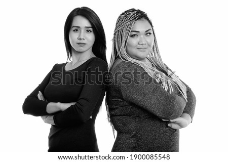 Studio shot of young Asian transgender woman and fat Asian woman with arms crossed together with back to back