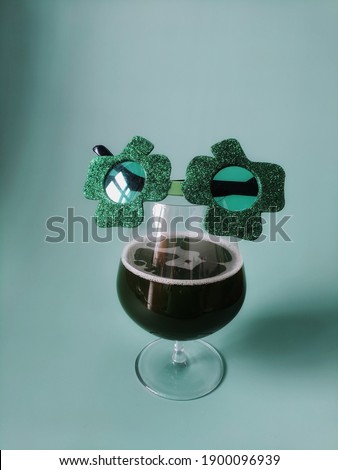 Happy St Patrick's Day concept, March 17. Glass of green beer and party glasses in green background. Greeting card. Copy space. Top view. 