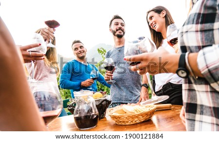 Friends group having fun together at garden party - Young people enjoying harvest time drinking red wine at farm house vineyard - Friendship concept with men and women outside on warm sunset filter