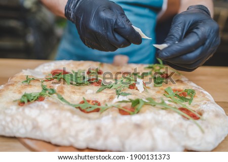 Chef hands in black gloves putting parmesan cheese on top of a pizza