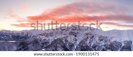 Drone shot, over frozen valley, in front of snowy, mountain peaks and sunset colors