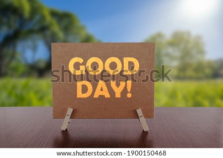 Good day text on card on the table with sunny green park background. 