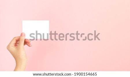 Woman hand holding blank white business card, discount or flyer on pink background with copy space. Template for your design